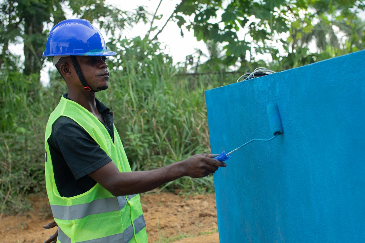 A worker applies a vibrant shade of blue to the wall of the new toilet block.